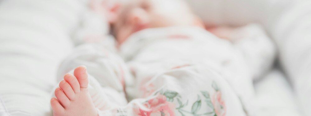 Baby in White and Red Floral Onesie Lying On Bed