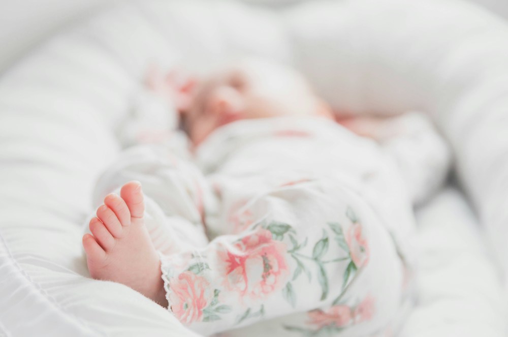 Baby in White and Red Floral Onesie Lying On Bed